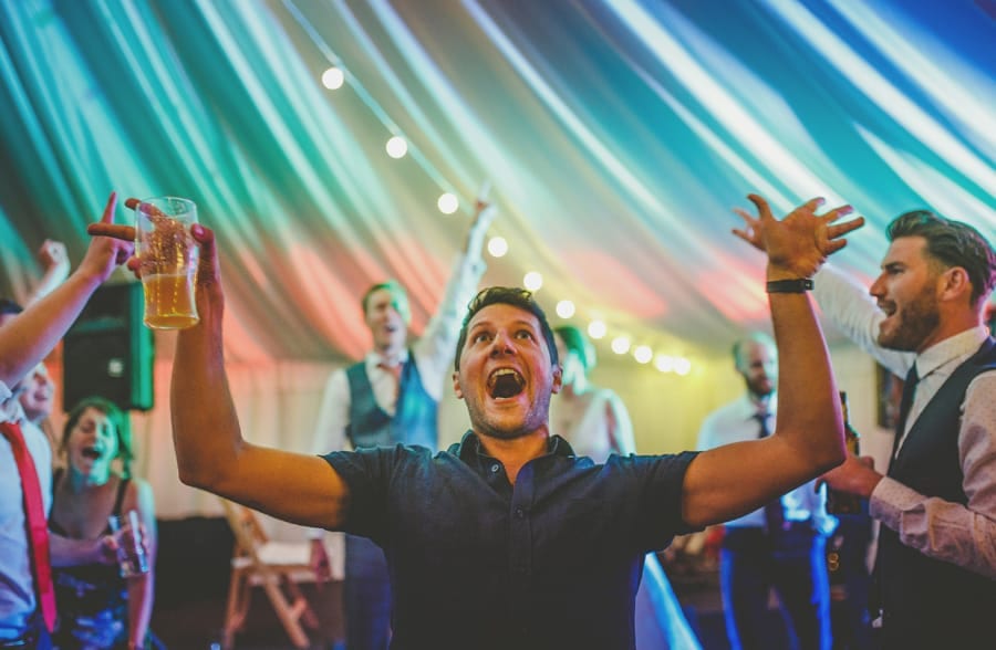 A wedding guest holds an alcoholic drink and looks up to the roof of the marquee