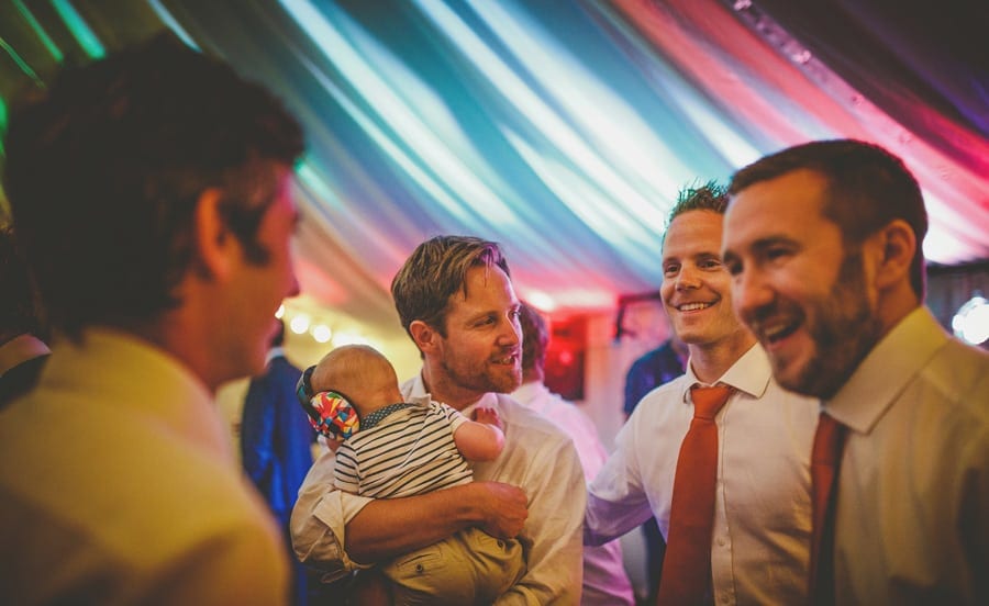 A wedding guest holds his baby in his arms and chats with friends in the marquee