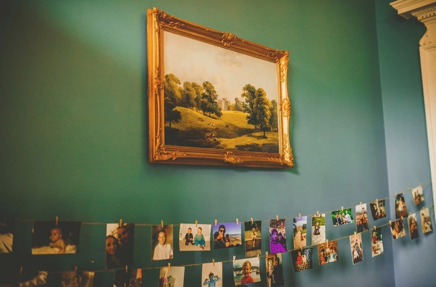 An oil painting hangs from a wall with photographs of the bride and groom hanging from string