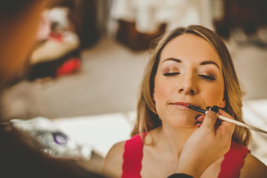 The bride has lipstick applied onto her lips by the makeup artist