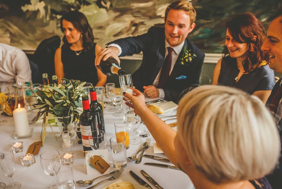 A wedding guest pours wine into a ladies glass as they sit around the wedding table