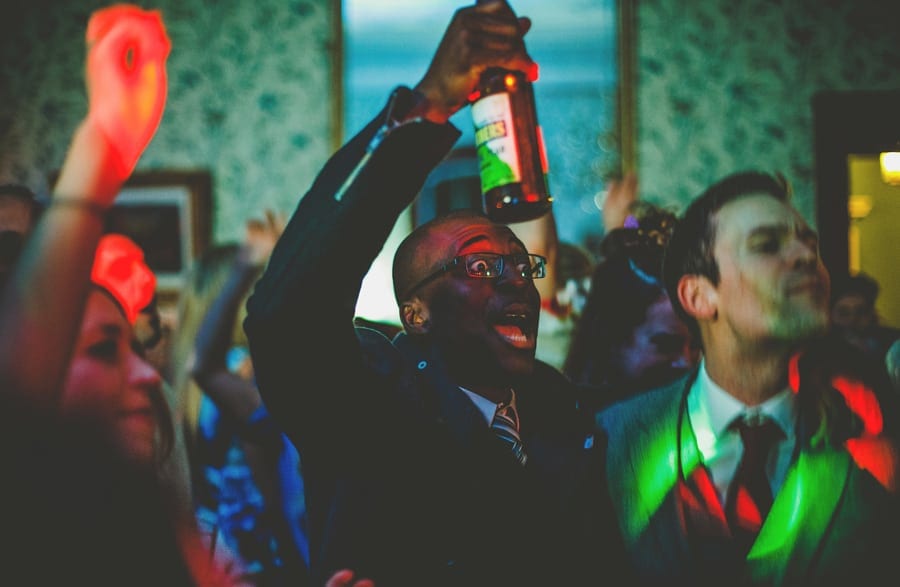 A wedding guest holds up a bottle of beer in his right hand on the dancefloor