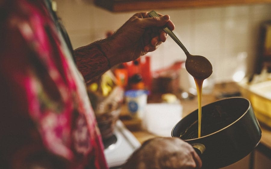 Little Quarme wedding photographer 0004 | somerset-wedding-photographer A wedding guest drips treacle from a spoon into a large pan in the kitchen of one of the cottages