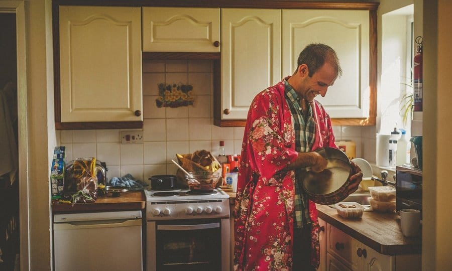Little Quarme wedding photographer 0007 | somerset-wedding-photographer A man wearing a red silk nightgown cleans a baking tray in the kitchen