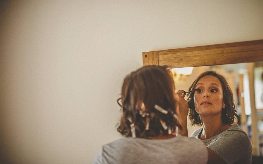 Little Quarme wedding photographer 0009 | somerset-wedding-photographer A bridesmaid puts eyeliner on her eyelashes as she looks into a large mirror hanging from a wall