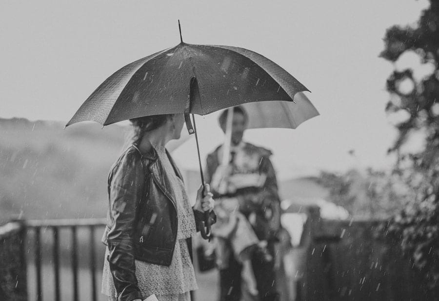Little Quarme wedding photographer 0038 | somerset-wedding-photographer A wedding guest holds an umbrella over her head as the rain falls