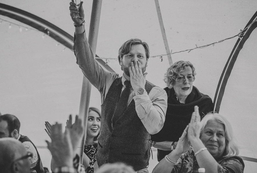Little Quarme wedding photographer 0053 | somerset-wedding-photographer A wedding guest puts his fingers to his lips and raises a glass of champagne in the outdoor marquee