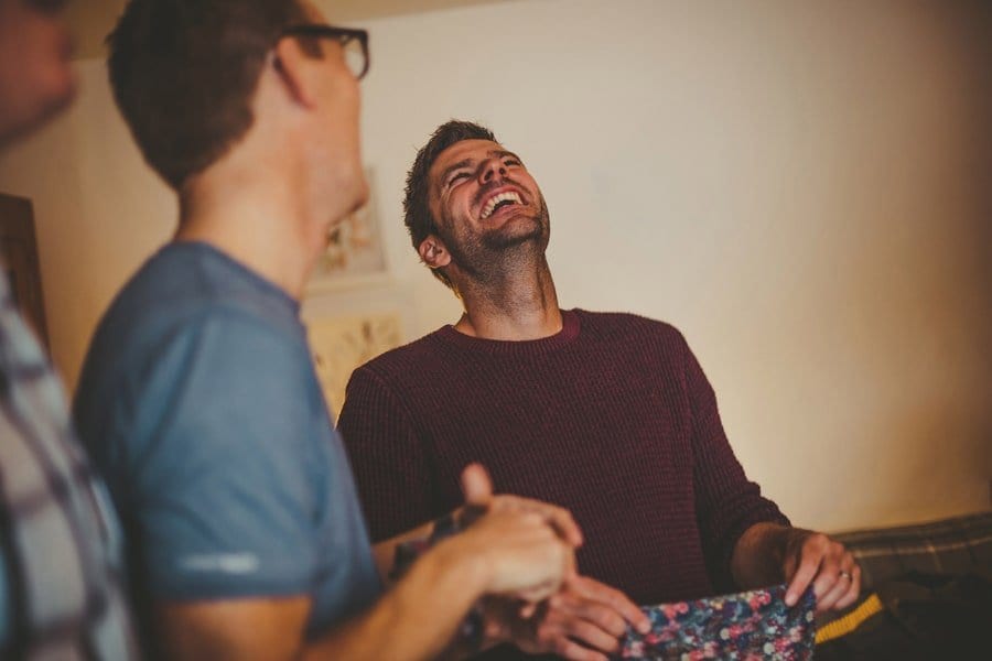 A man looks up at the ceiling and laughs as he opens his present