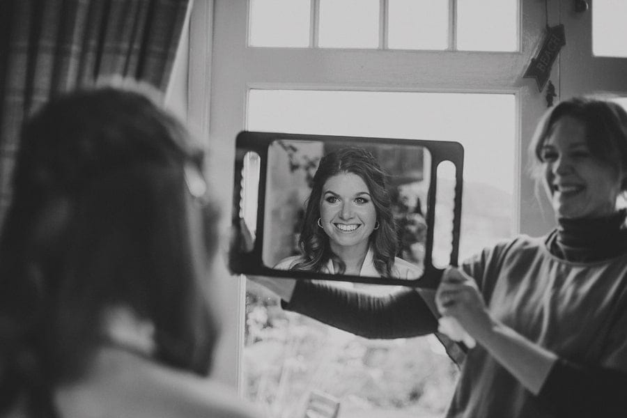 The bride looks into a mirror held by the make up artist and smiles at herself