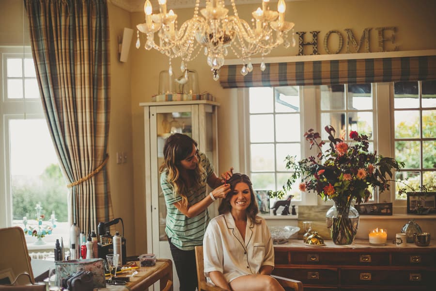 The bride sits down and has her hair tied back by the hairdresser