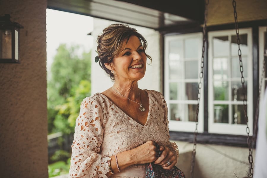The brides mother smiles at her husband as they stand outside their house