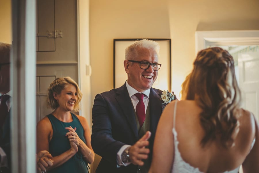 The bride's father puts his arms around his daughter and smiles at her