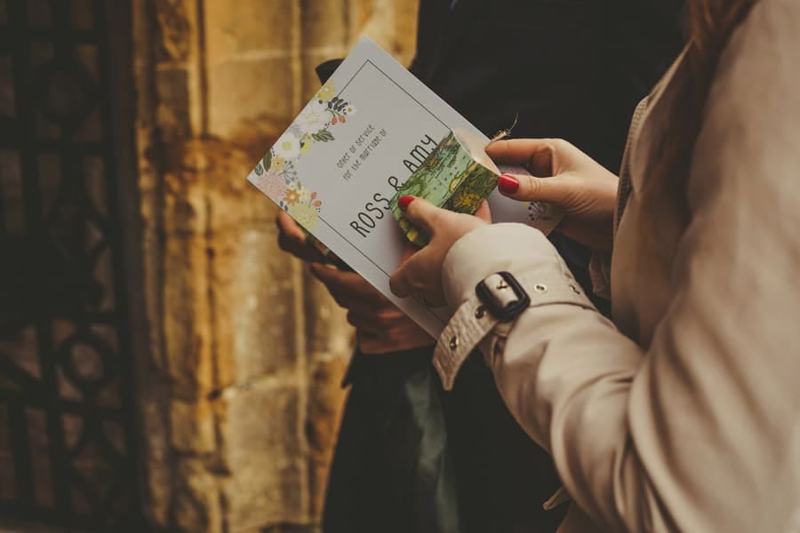 A wedding guest holds an order of service and a small box as she walks into the Church