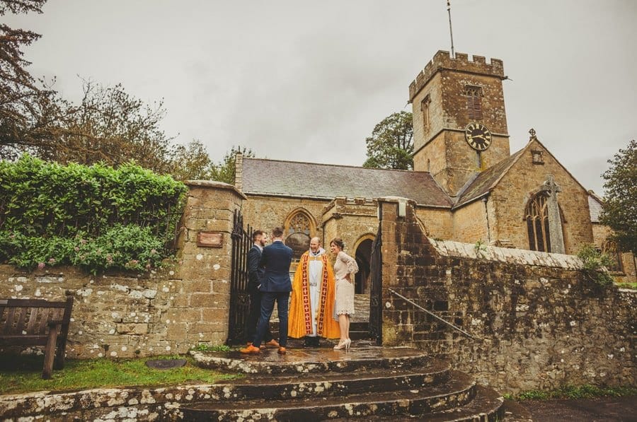 The vicar stands outside the Church and talks to the brides mother and the ushers