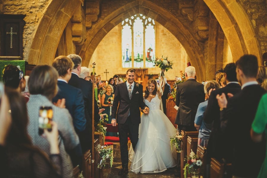 The bride raises her bouquet in the air as she holds the grooms hand in the Church