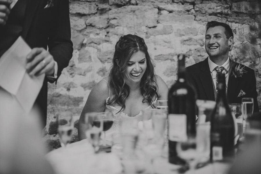 The bride sits at the table and laughs at her father's wedding speech