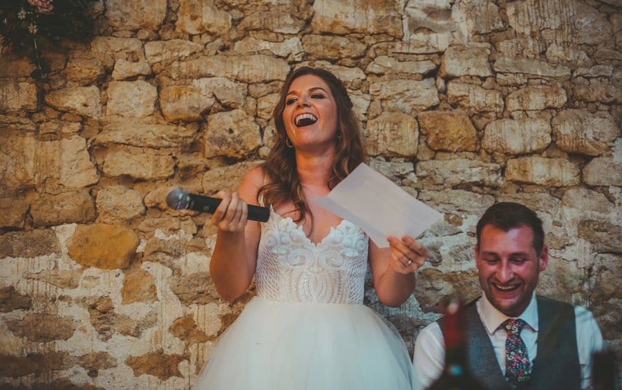 The bride stands up and speaks in front of the wedding guests with a microphone in one hand and a piece of paper in the other hand