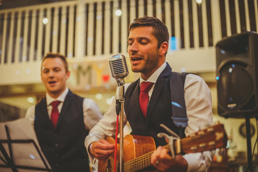 An usher plays a guitar and sings a song to the wedding party