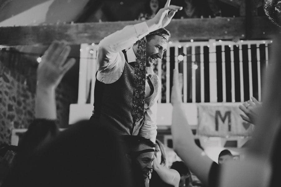 The groom raises his hand in the air while the ushers lift him over their shoulders