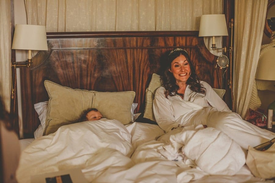 The bride sits in bed with her niece looking out under the covers