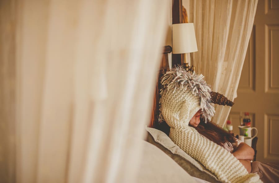 The bride sits on the bed with a woven hat on