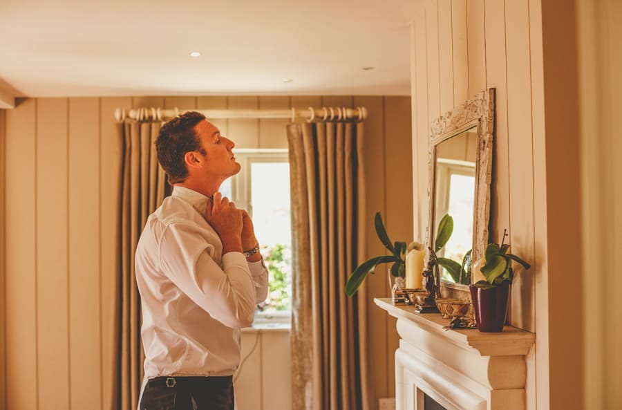 An usher straightens the collars of his shirt as he looks into the mirror hanging from a wall in the house