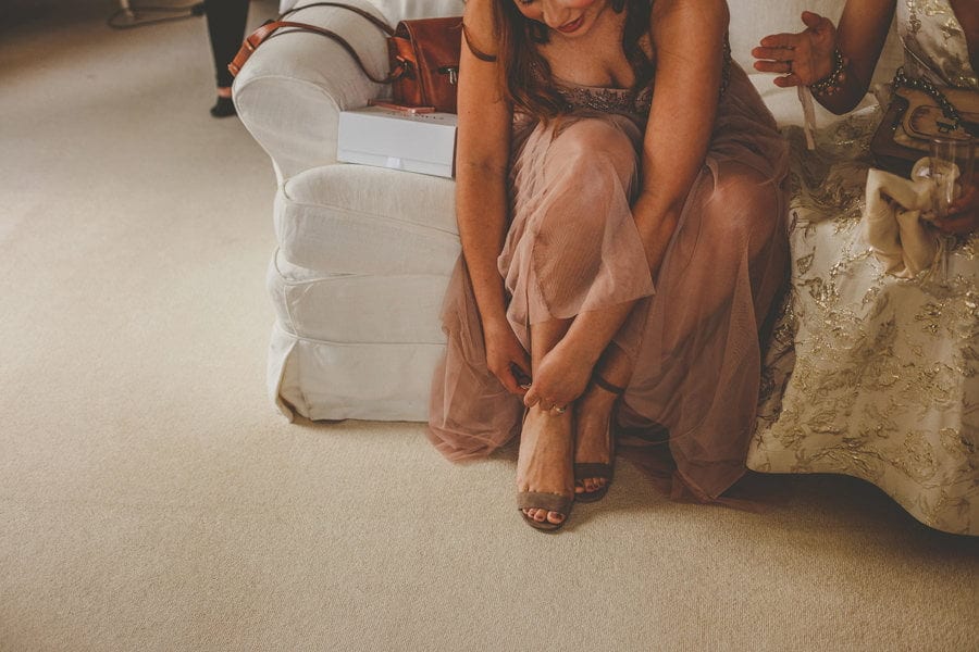 A bridesmaid sits on a sofa and fastens her new shoes