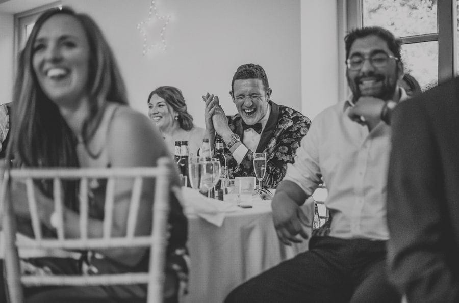 The best man laughs as he sits at a table with friends during the grooms speech