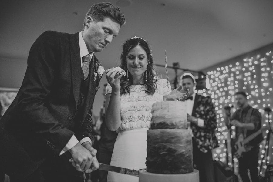 The bride puts a piece of wedding cake into her own mouth and watches her husband cut the wedding cake