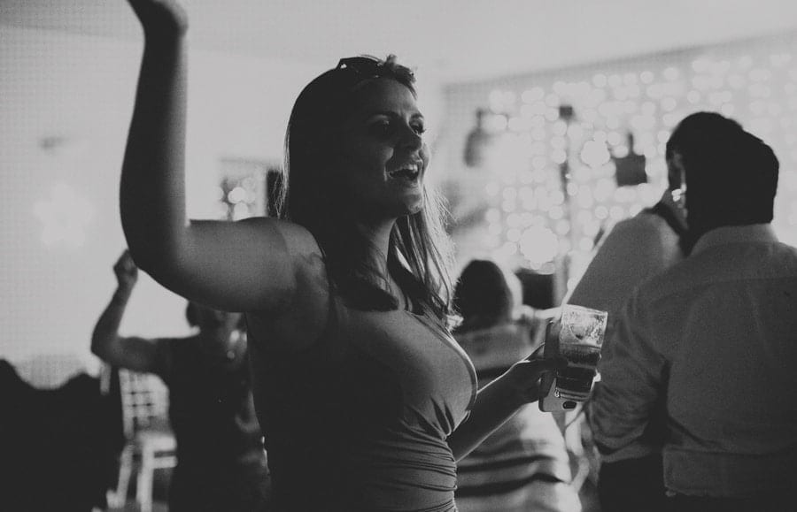A wedding guest holds a drink in one hand and dances