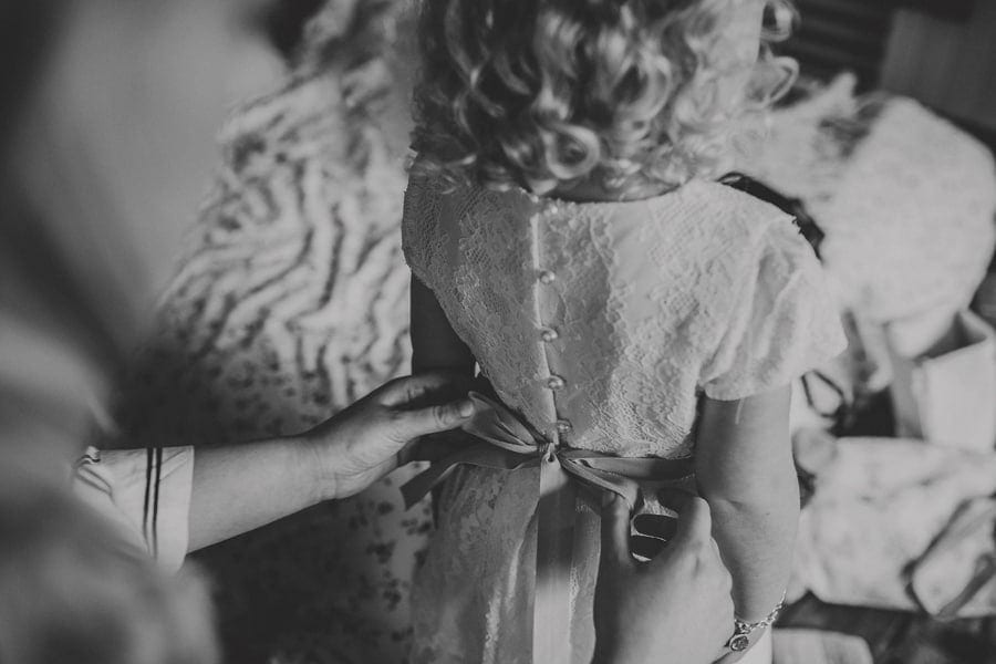 The bride ties the flower girls straps on the back of her dress at Over Barn
