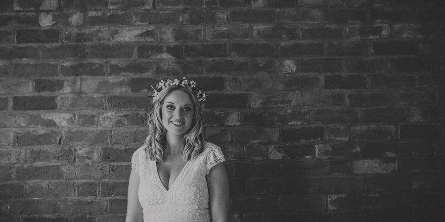 The bride posing for a photograph against a large brick wall