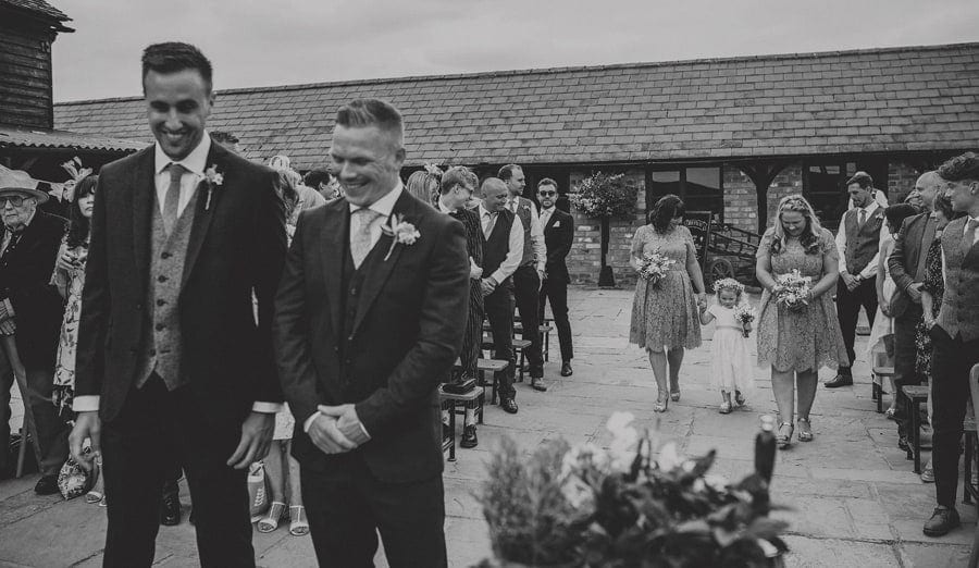 The bridesmaids and flower girl walk down the aisle in the courtyard at Over Barn