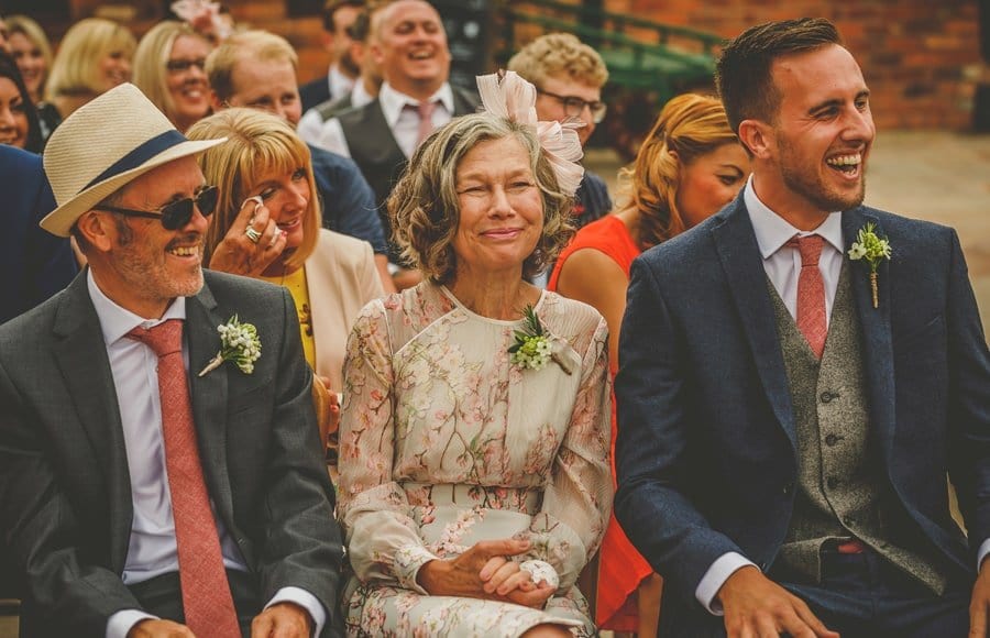 The grooms mother and father and the best man laugh during the outdoor wedding ceremony