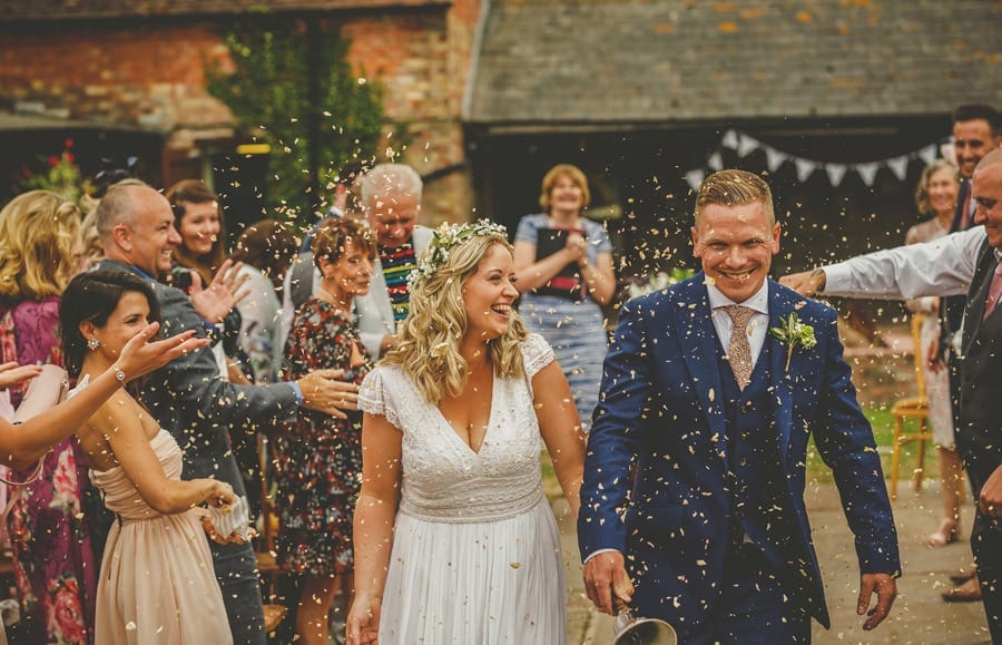 The bride and groom walk down the aisle together and are showered in confetti that is thrown by wedding guests at Over Barn in Gloucestershire