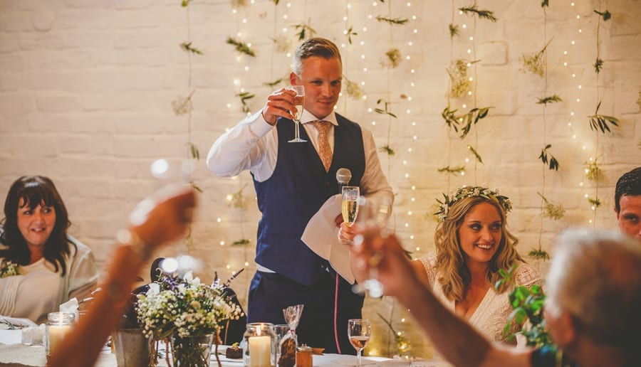 The groom raises his glass with friends and family as he makes a toast to his wife in the barn