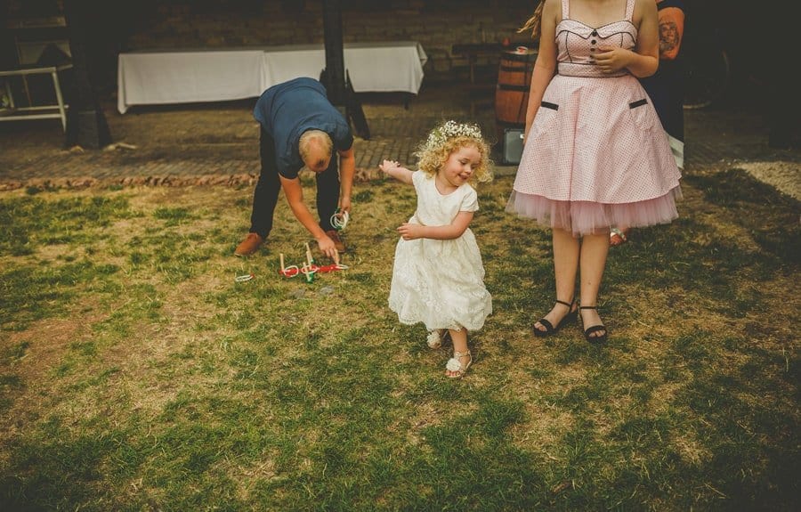 The bride and grooms daughter plays on the grass in the courtyard with her friends and family