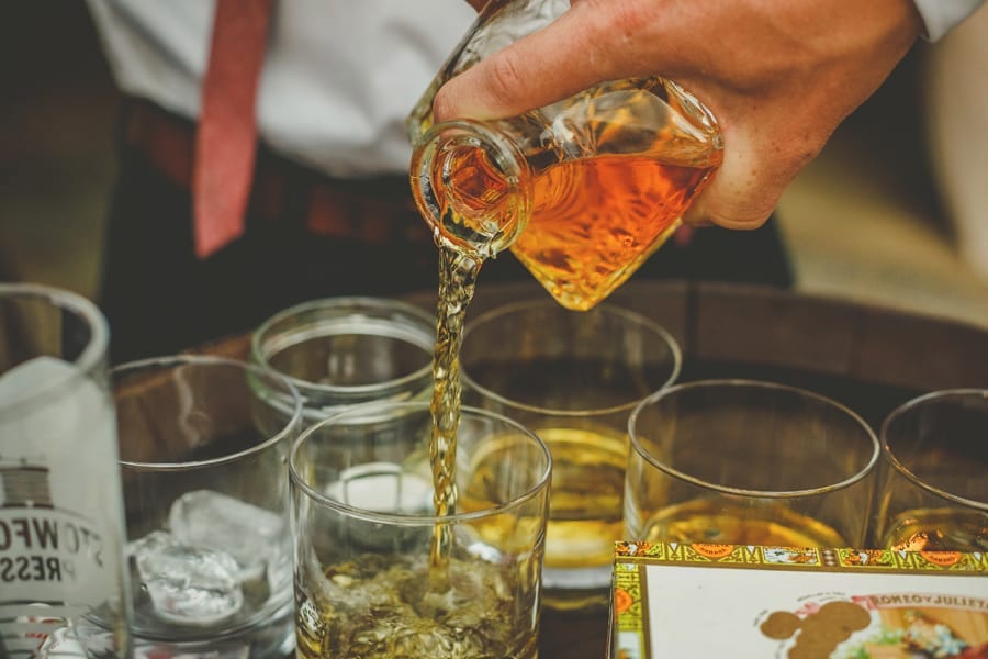 The groom pours brandy into glasses in the courtyard at Over Barn