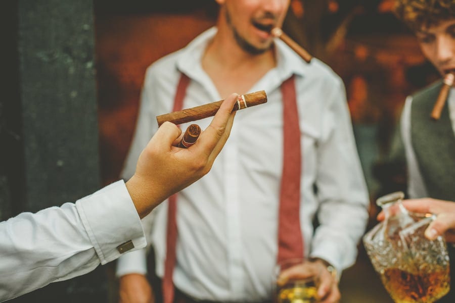 A man offers a cigar to his friend in the courtyard