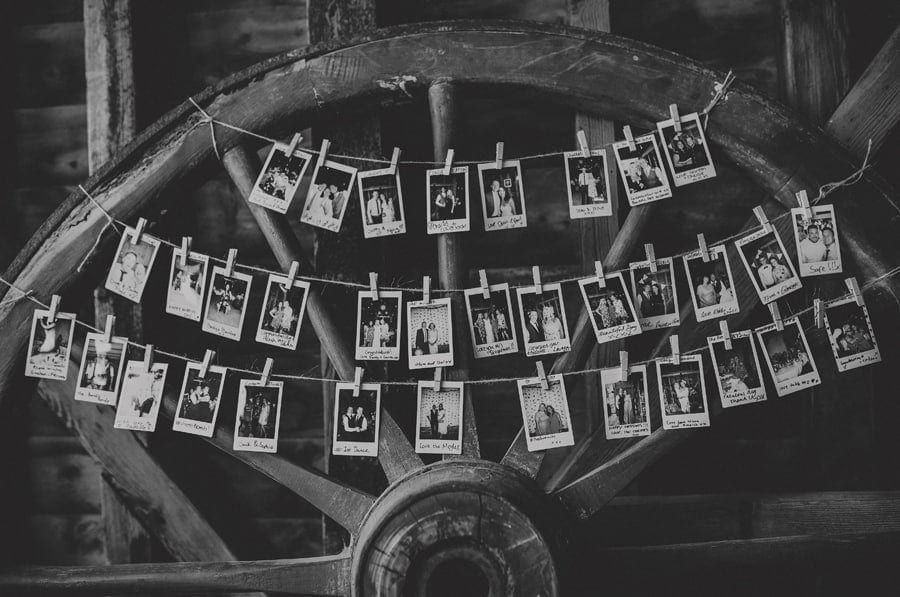 Polaroid photographs hang from string against an old large wooden tractor wheel in the barn