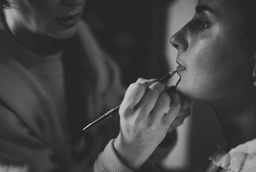 The makeup artist applies lipstick onto the lips of the bride in the cottage in Frome