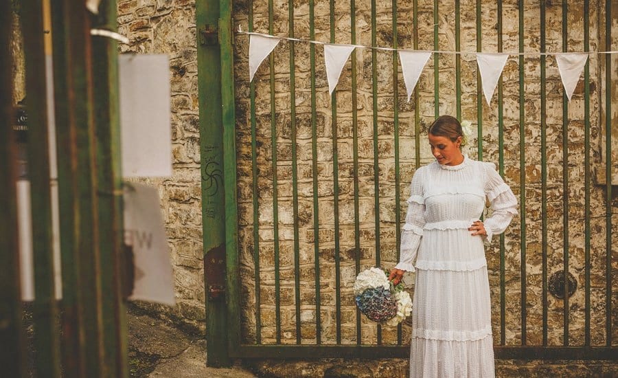 The bride holds her bouquet in her right hand and stands in front of the main gate at Silk Mill Studios in Frome