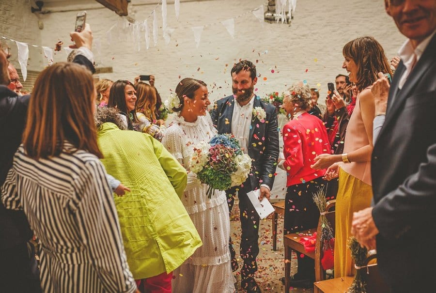 The bride and groom are showered with confetti as they walk down the aisle after the wedding ceremony at Silk Mill studios in Frome