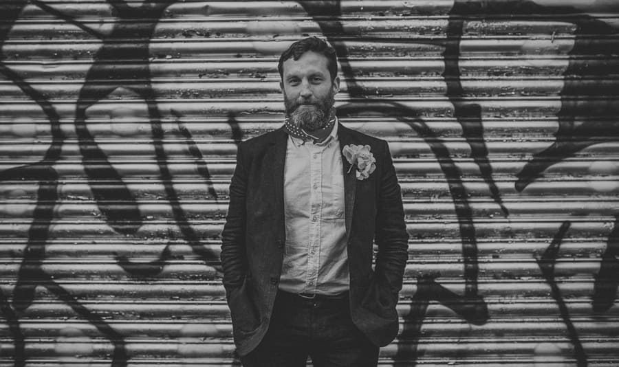 The groom poses for a photograph in front of a large metal shutter