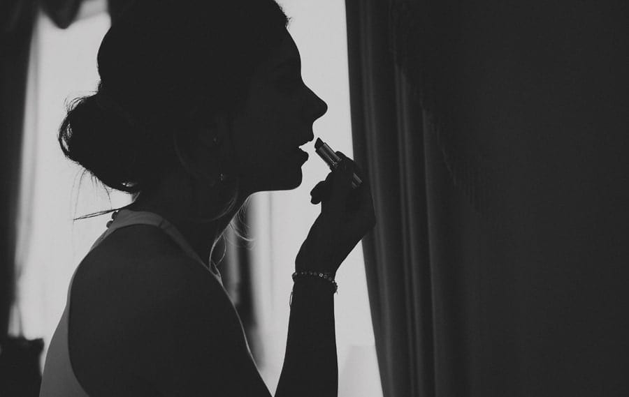 A bridesmaid applies lipstick on her lips in the Master bedroom at Stubton Hall