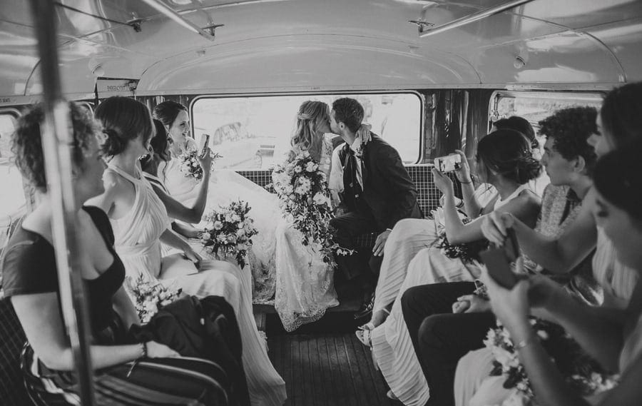 The bride and groom sit on the back of the wedding bus and share a kiss with each other