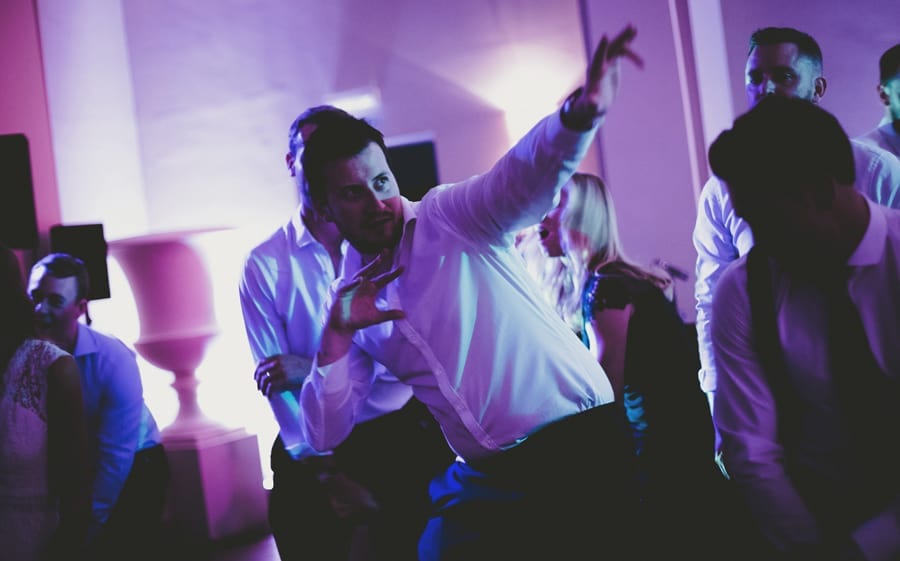 A wedding guest raises his arm and points to the ceiling on the dancefloor