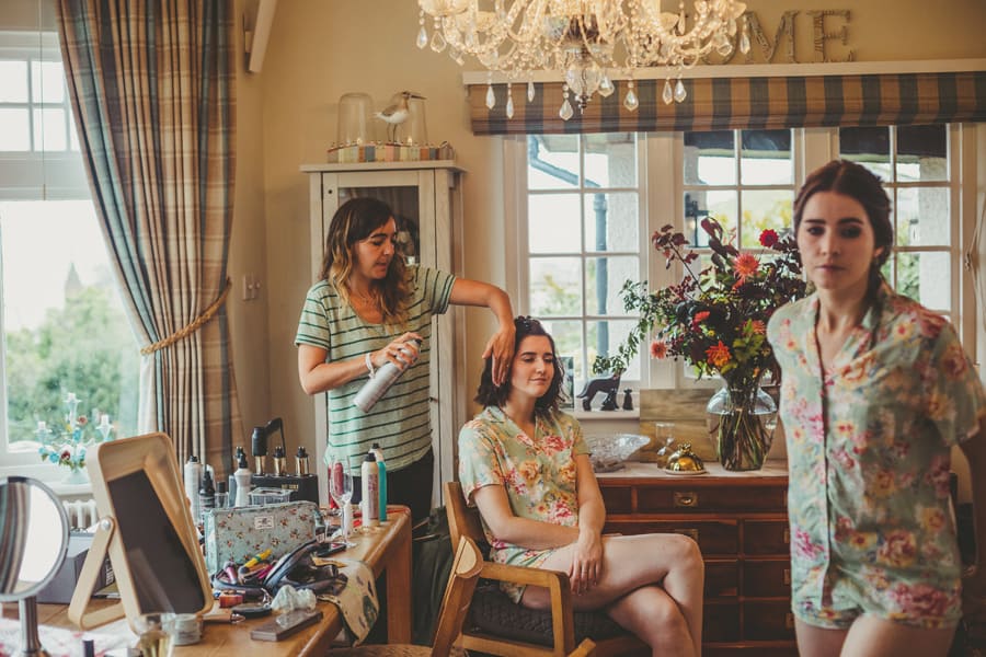 A hairdresser sprays hair spray on the hair of a bridesmaid