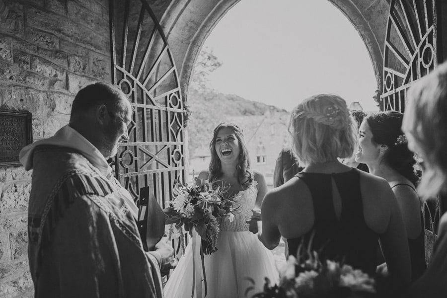The bride shares a joke with the vicar at the door of the Church with the wedding party