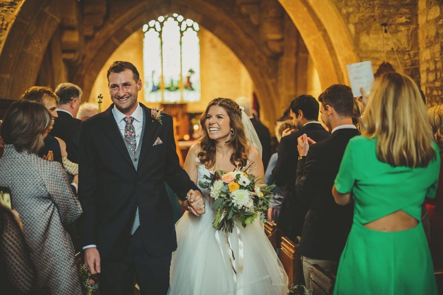 The bride and groom smile to wedding guests as they walk down the aisle of the Church